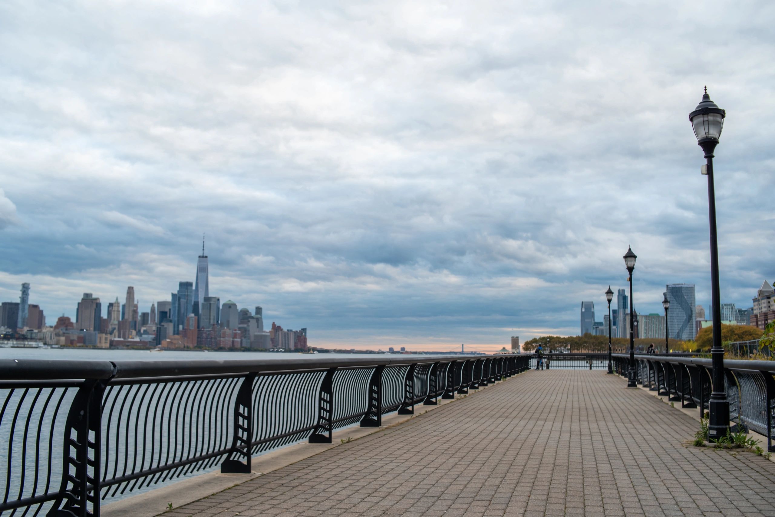 One World Trade Center and the Lower Manhattan skyline viewed from the Hoboken, New Jersey waterfront promenade on a cloudy autumn day.